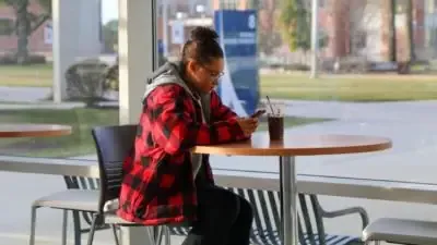 Student texting on campus while drinking coffee.